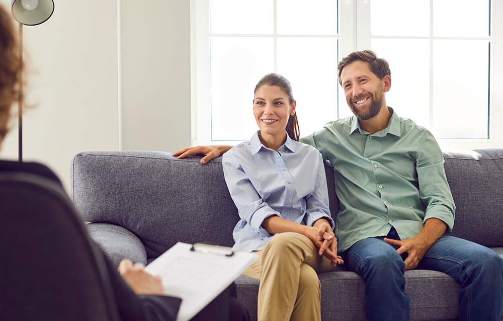 Young,Smiling,Couple,Sitting,On,Sofa,And,Talking,With,Psychologist